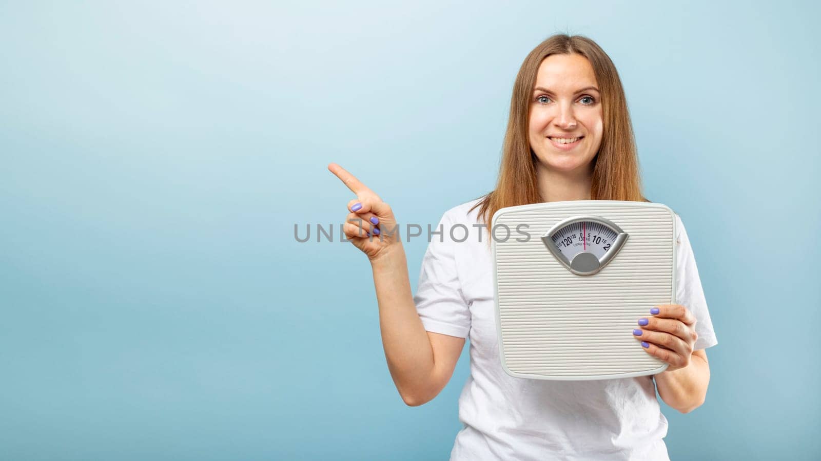 Beautiful young caucasian woman holding weight machine (scale) to balance weight loss pointing with finger to empty space for ypur text or object.