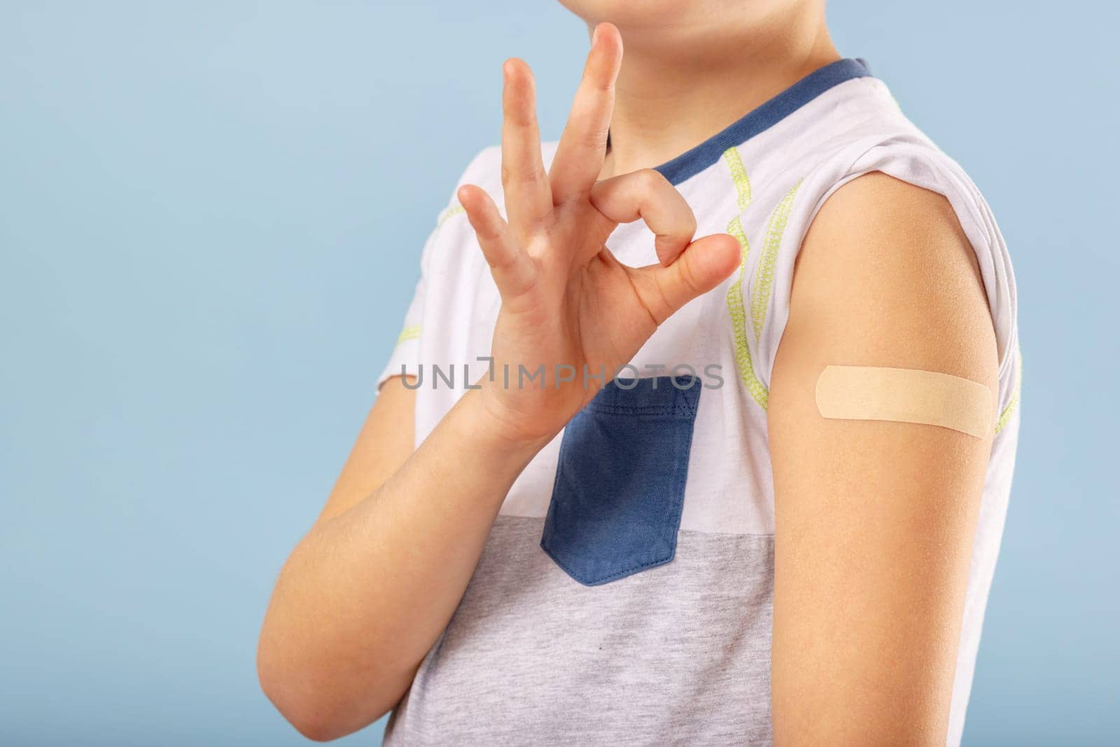 Vaccination of children. Happy vaccinated kid boy is gesturing okay and showing arm with adhesive bandage after vaccine injection. Kids and covid-19 prevention, antiviral immunization.