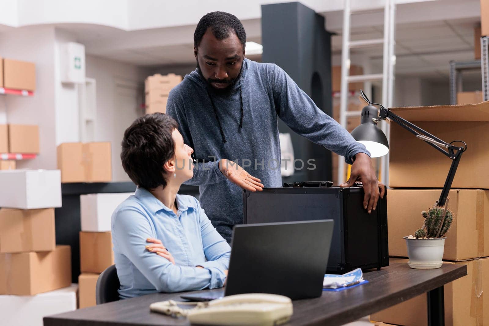 Workers discussing about metallic box while checking transportation logistics for package delivery on laptop computer. Storehouse manager analyzing online shipping order working in warehouse