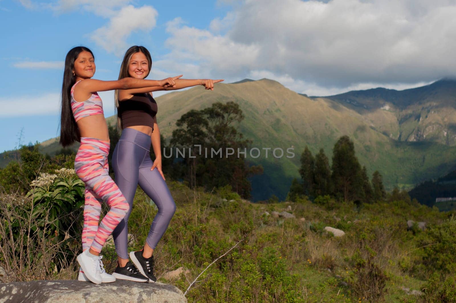 Portrait of a mother and her daughter in sportswear standing in the mountains pointing to the right at a copy space.