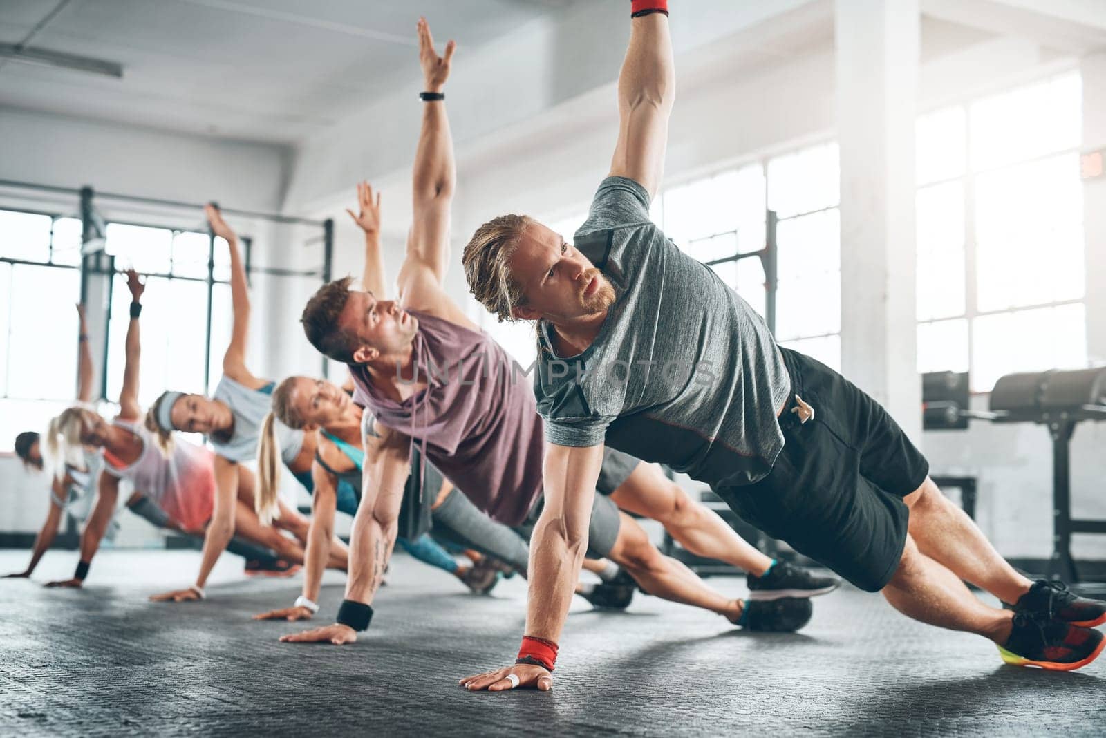 Gym class, group and athletes doing a workout for fitness, health or wellness flexibility. Sports, community and people doing a side plank exercise, training or challenge together in a sport studio