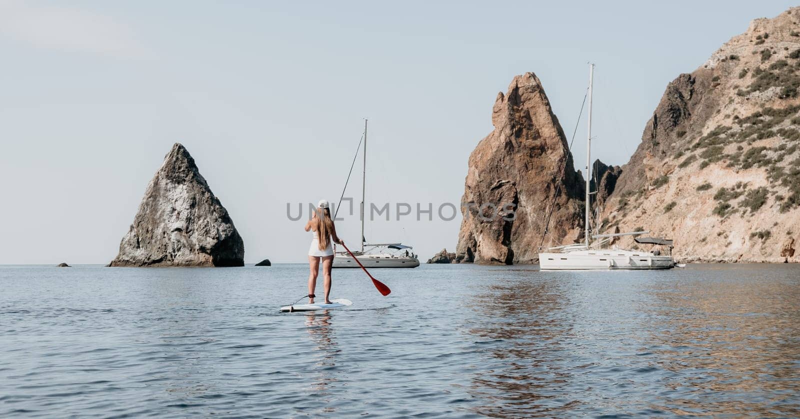 Close up shot of beautiful young caucasian woman with black hair and freckles looking at camera and smiling. Cute woman portrait in a pink bikini posing on a volcanic rock high above the sea