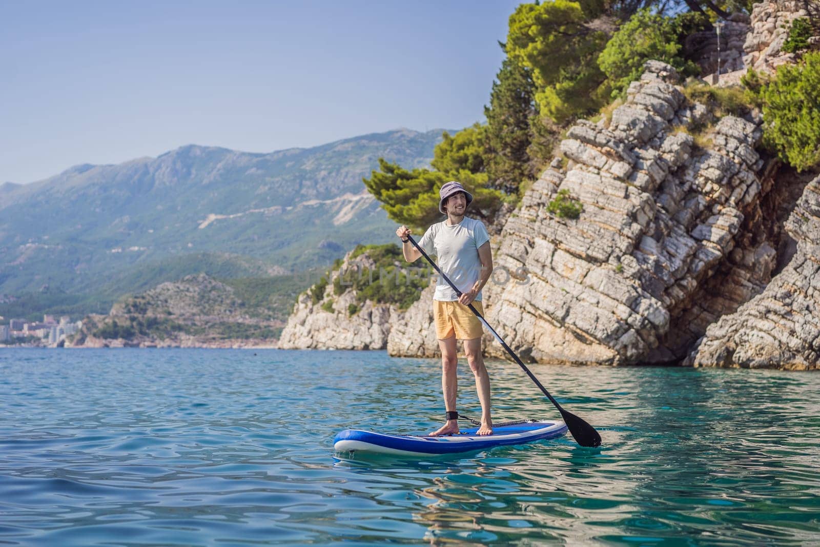 Young men Having Fun Stand Up Paddling in blue water sea near st stefan island against the backdrop of Milocer Park in Montenegro. SUP by galitskaya