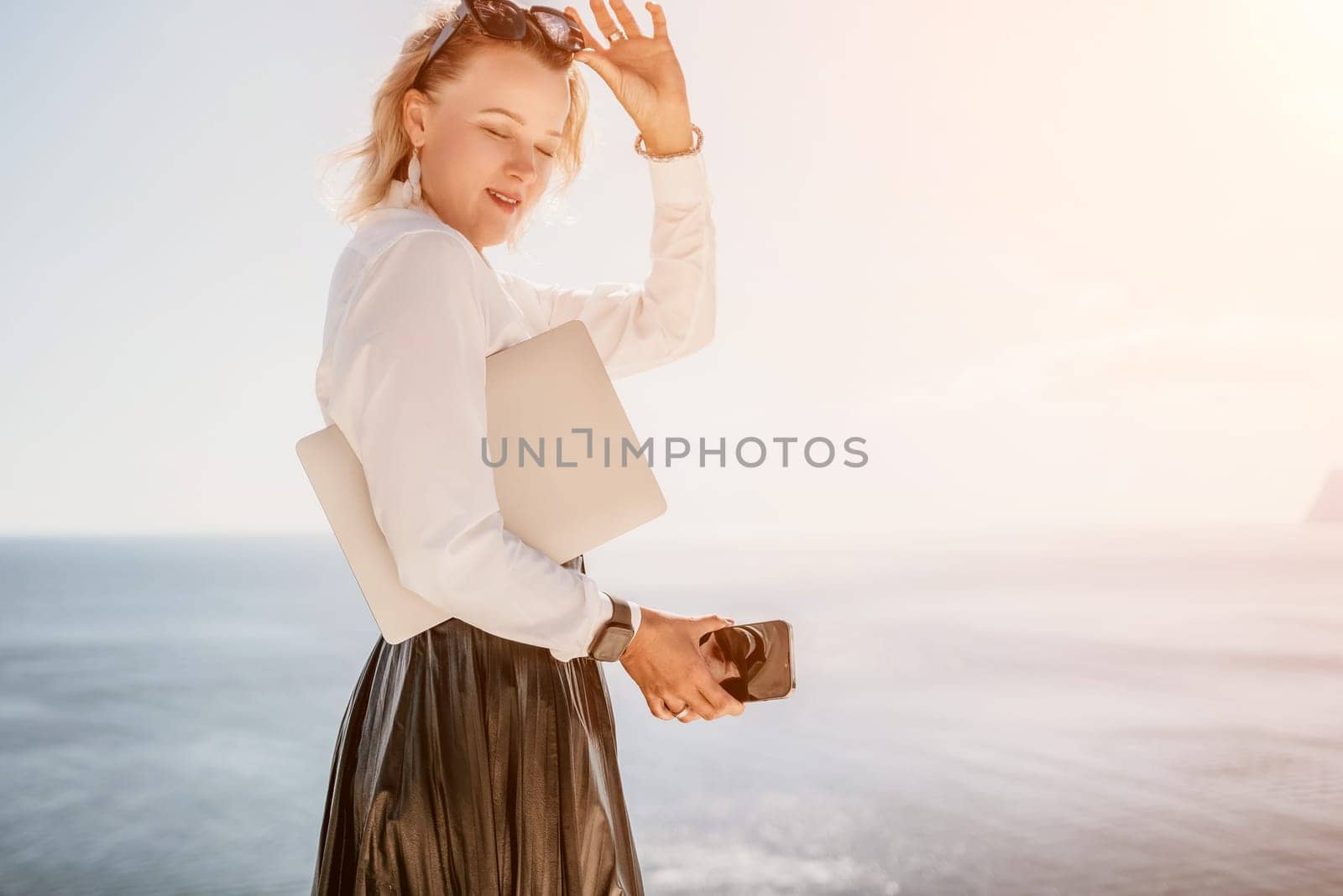 Digital nomad, Business woman working on laptop by the sea. Pretty lady typing on computer by the sea at sunset, makes a business transaction online from a distance. Freelance remote work on vacation