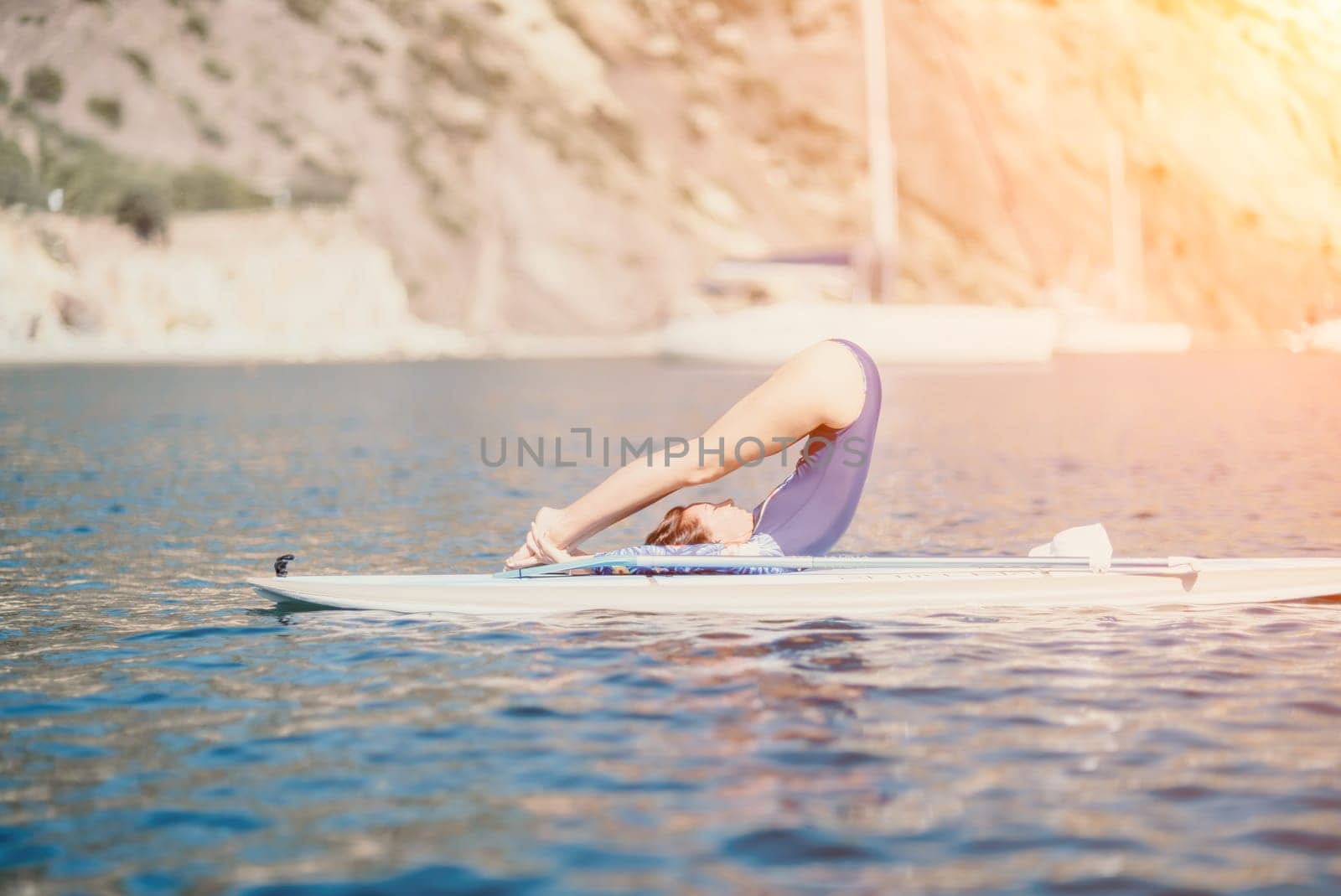 Woman sup yoga. Middle age sporty woman practising yoga pilates on paddle sup surfboard. Female stretching doing workout on sea water. Modern individual hipster outdoor summer sport activity