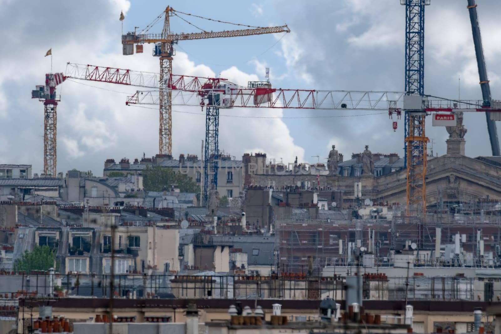 Rooftop telephoto shot of Paris skyline showing construction cranes, scaffolding, rooftop gardens, and chimneys of the iconic Haussmann apartment buildings. High quality photo