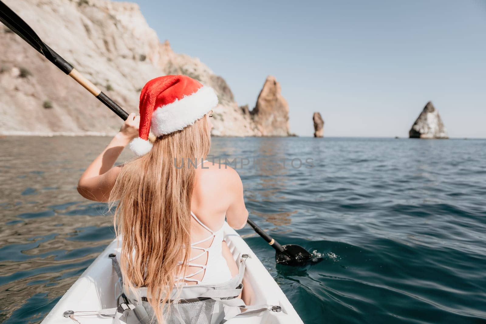 Woman in kayak back view. Happy young woman with long hair floating in transparent kayak on the crystal clear sea. Summer holiday vacation and cheerful female people relaxing having fun on the boat