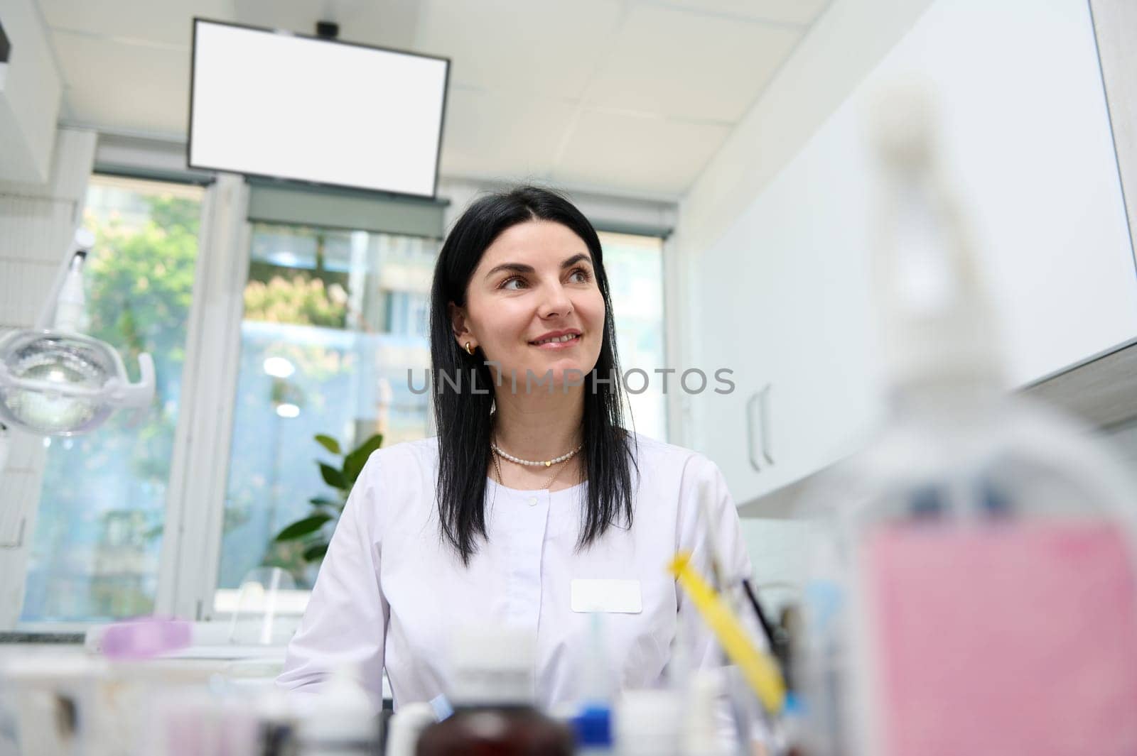 Portrait of smiling beautiful Caucasian woman 30s, experienced confident doctor dentist, dental technician, prosthetic engineer at workplace in dentist's office. Orthodontics Dentistry Dental practice