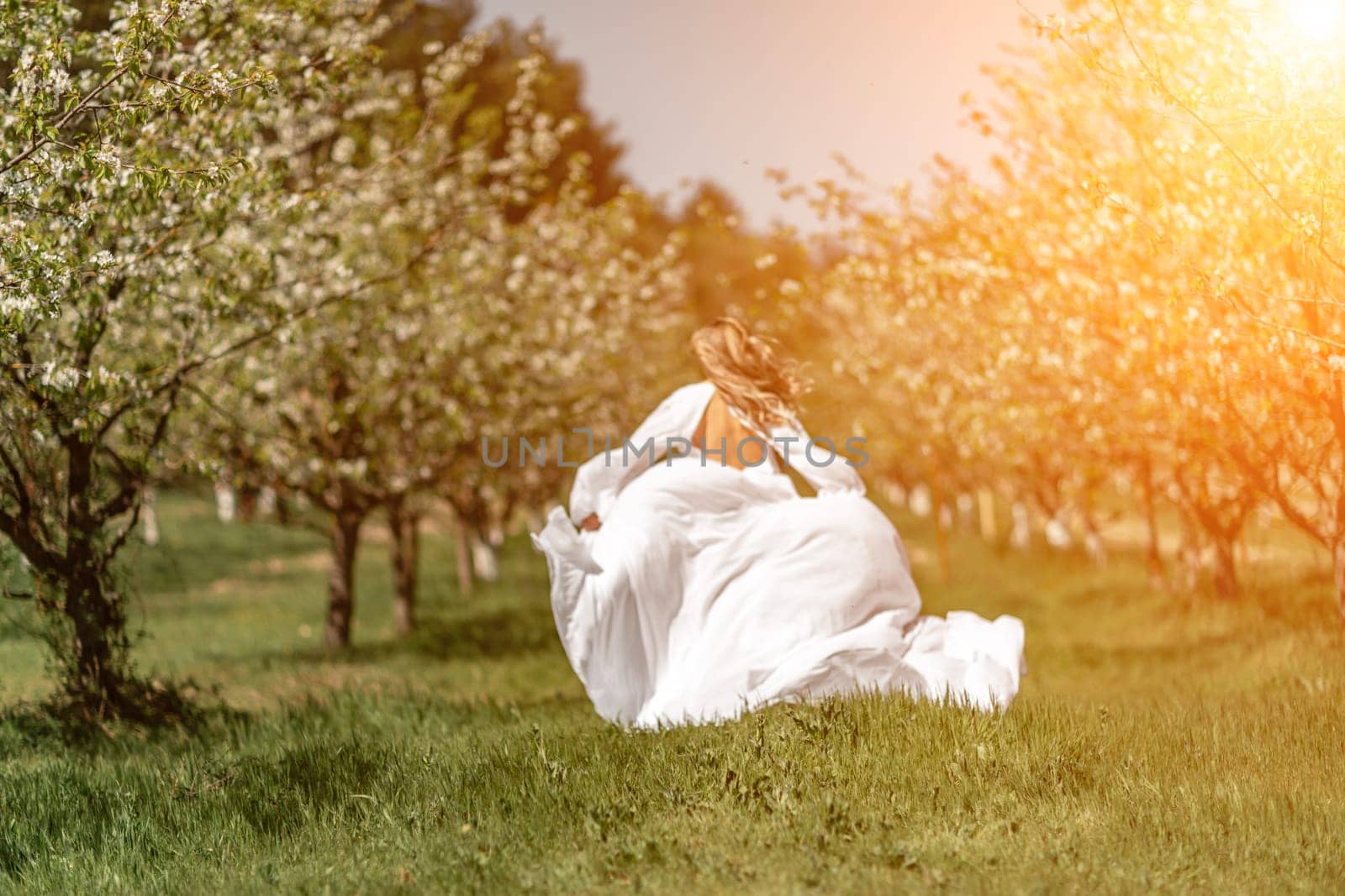 Woman white dress park. A woman in a white dress runs through a blossoming cherry orchard. The long dress flies to the sides, the bride runs rejoicing in life. by Matiunina