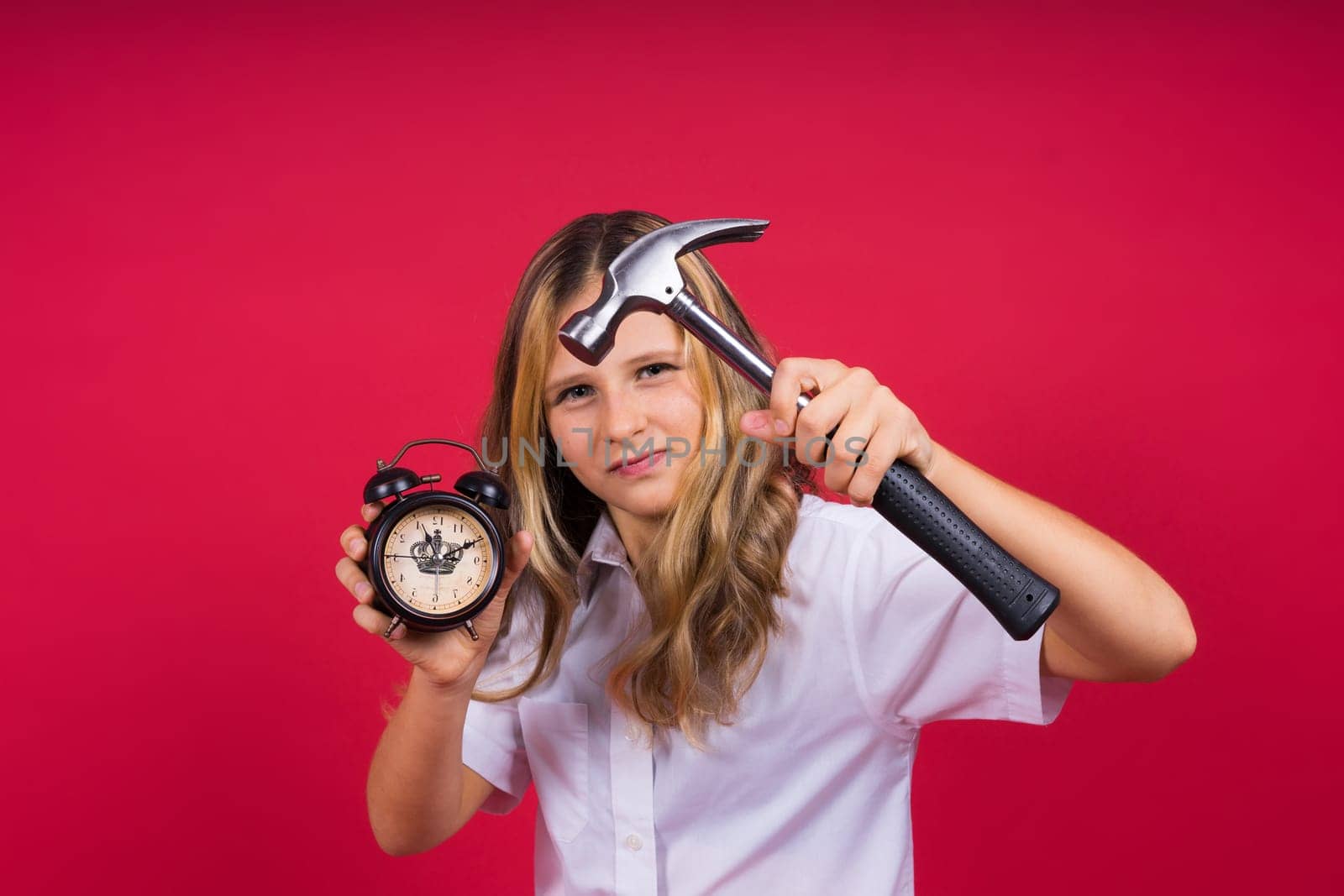 Young blonde girl holding an alarm clock and hammer smiling and laughing hard out loud.