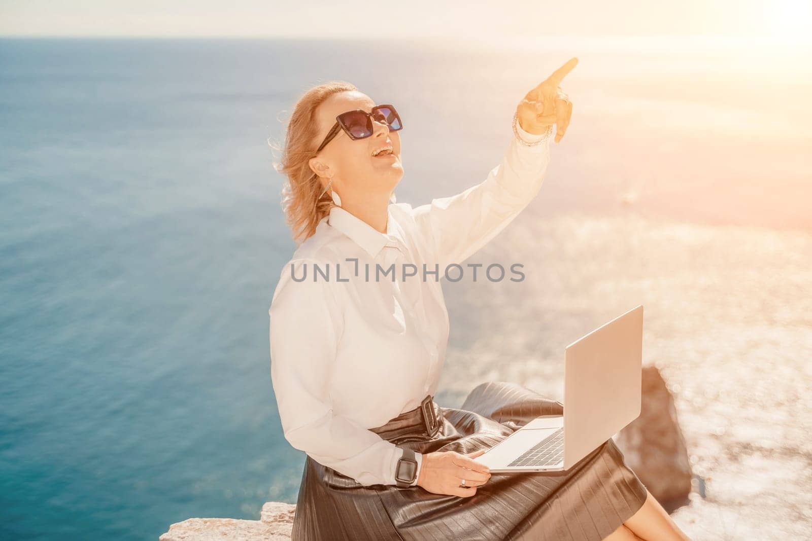 Business woman on nature in white shirt and black skirt. She works with an iPad in the open air with a beautiful view of the sea. The concept of remote work