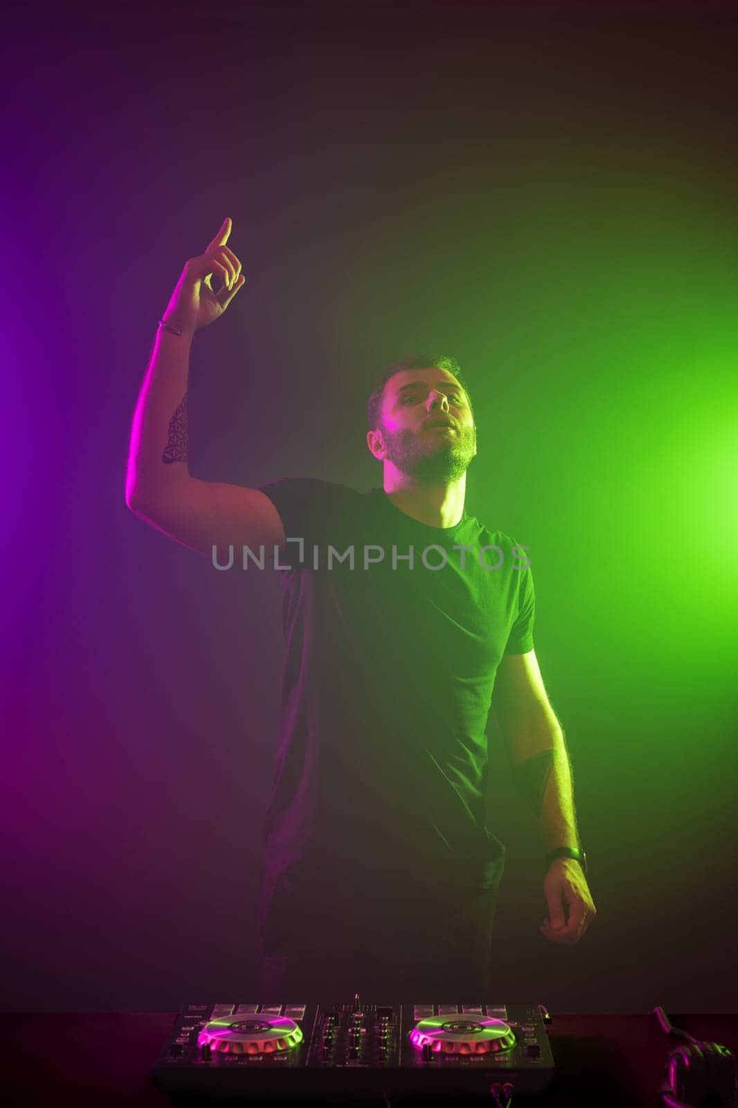 Handsome DJ in a black T-shirt at work mixing sound on her decks at a party or night club with colourful smoke light background