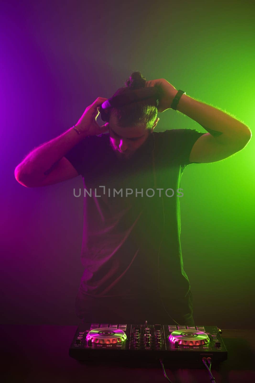 Handsome DJ in a black T-shirt at work mixing sound on her decks at a party or night club with colourful smoke light background