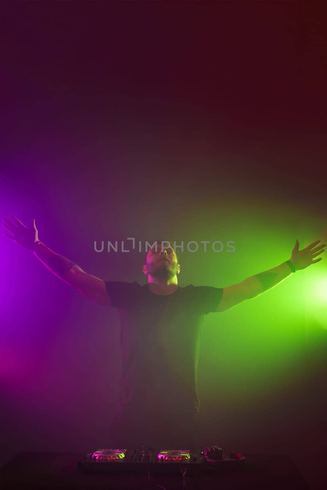 Handsome DJ in a black T-shirt at work mixing sound on her decks at a party or night club with colourful smoke light background