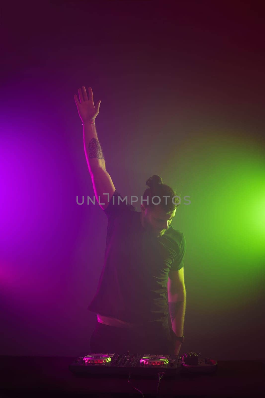 Handsome DJ in a black T-shirt at work mixing sound on her decks at a party or night club with colourful smoke light background