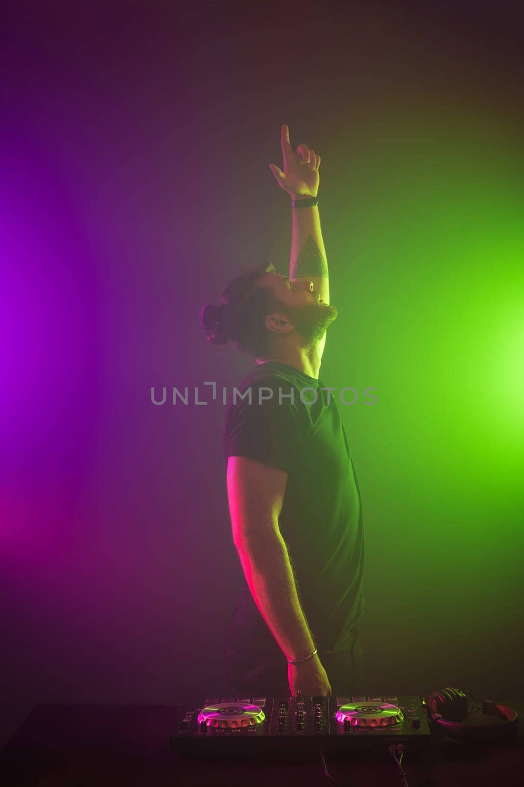 Handsome DJ in a black T-shirt at work mixing sound on her decks at a party or night club with colourful smoke light background