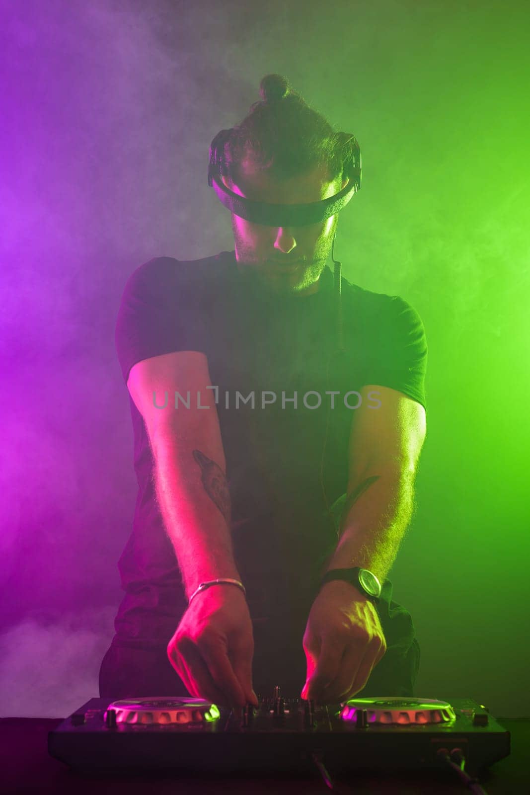 Handsome DJ in a black T-shirt at work mixing sound on her decks at a party or night club with colourful smoke light background