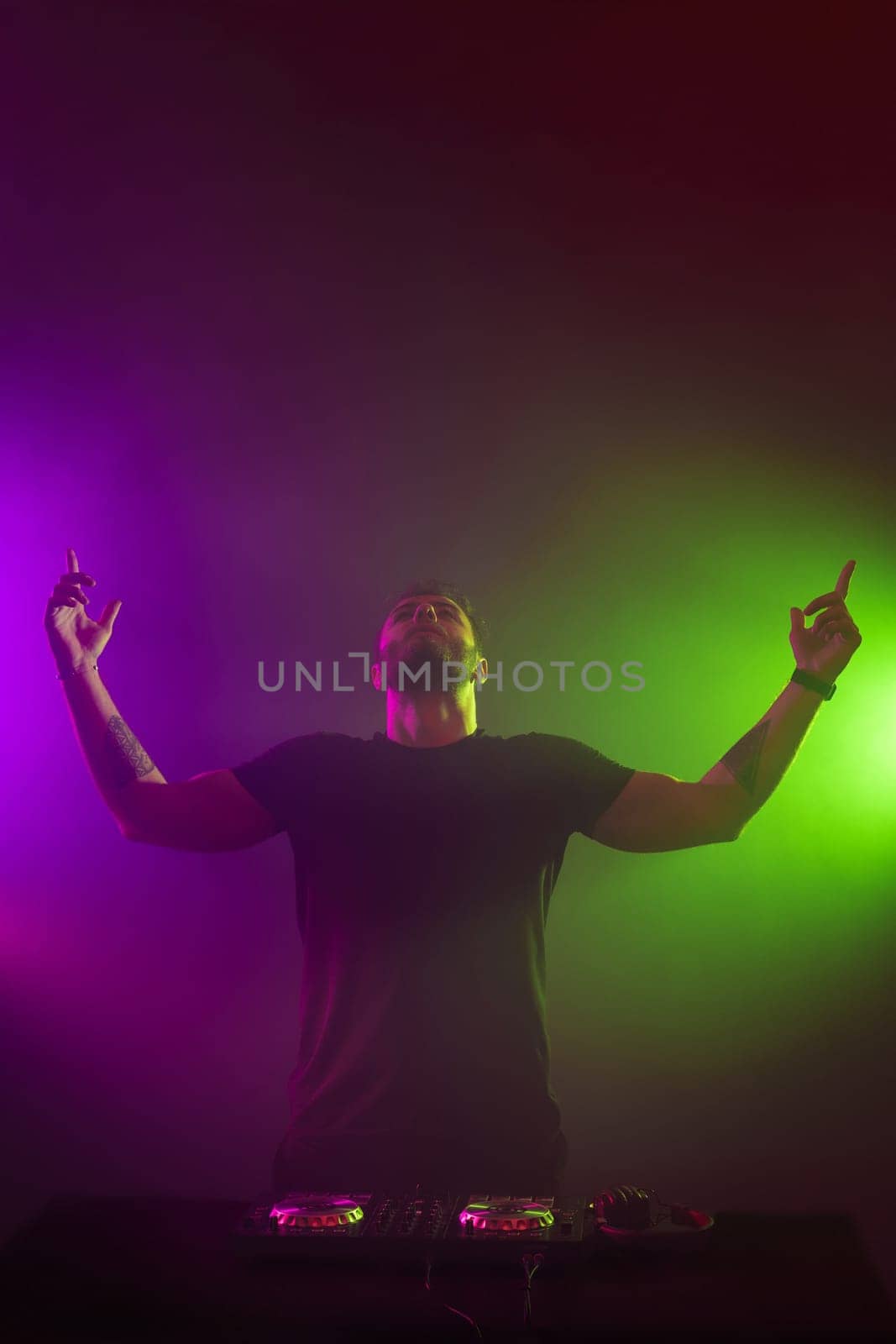 Handsome DJ in a black T-shirt at work mixing sound on her decks at a party or night club with colourful smoke light background