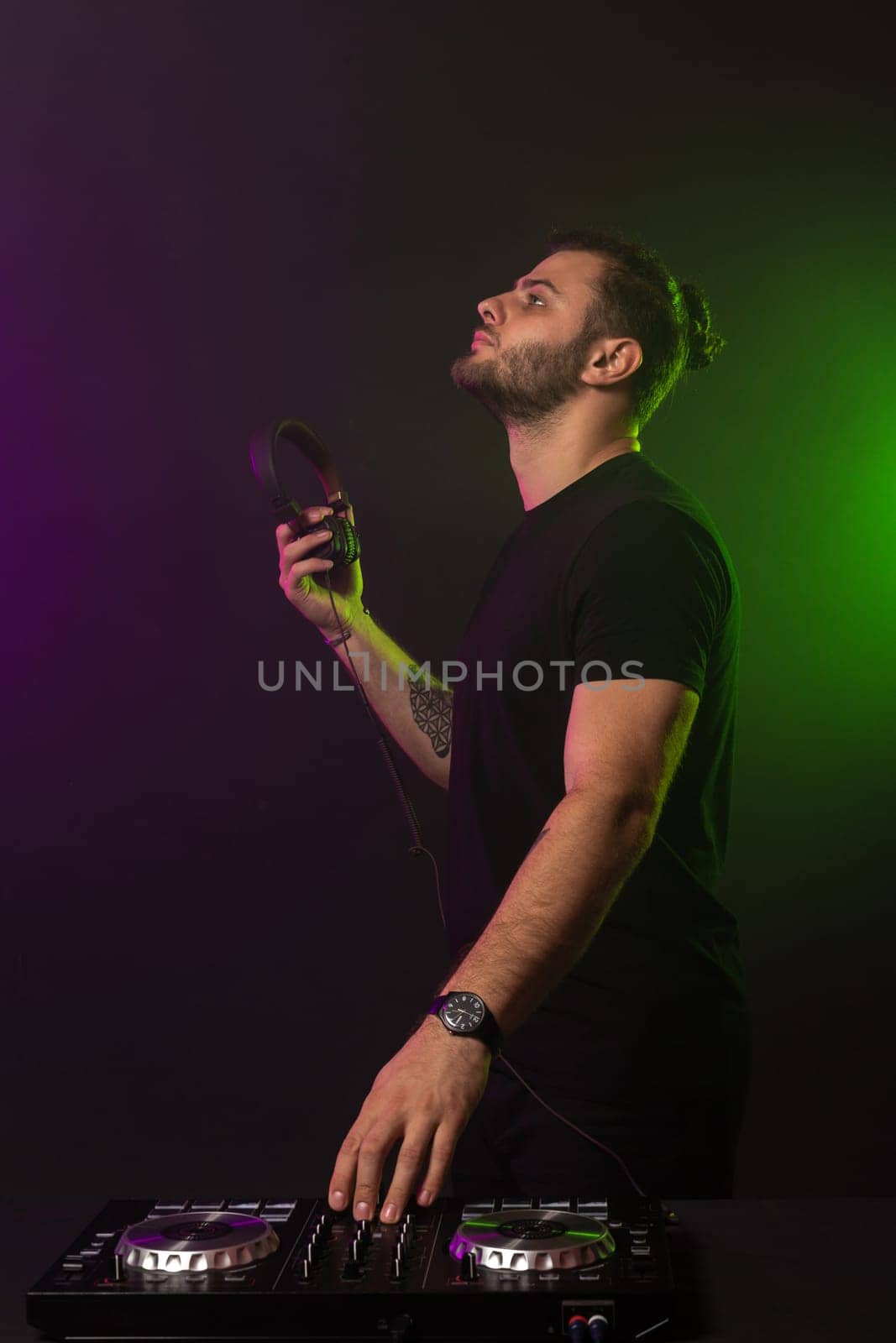 DJ playing music at mixer on colorful foggy background. A fashionable, handsome young man in a black T-shirt is behind the DJ's console. Studio shot