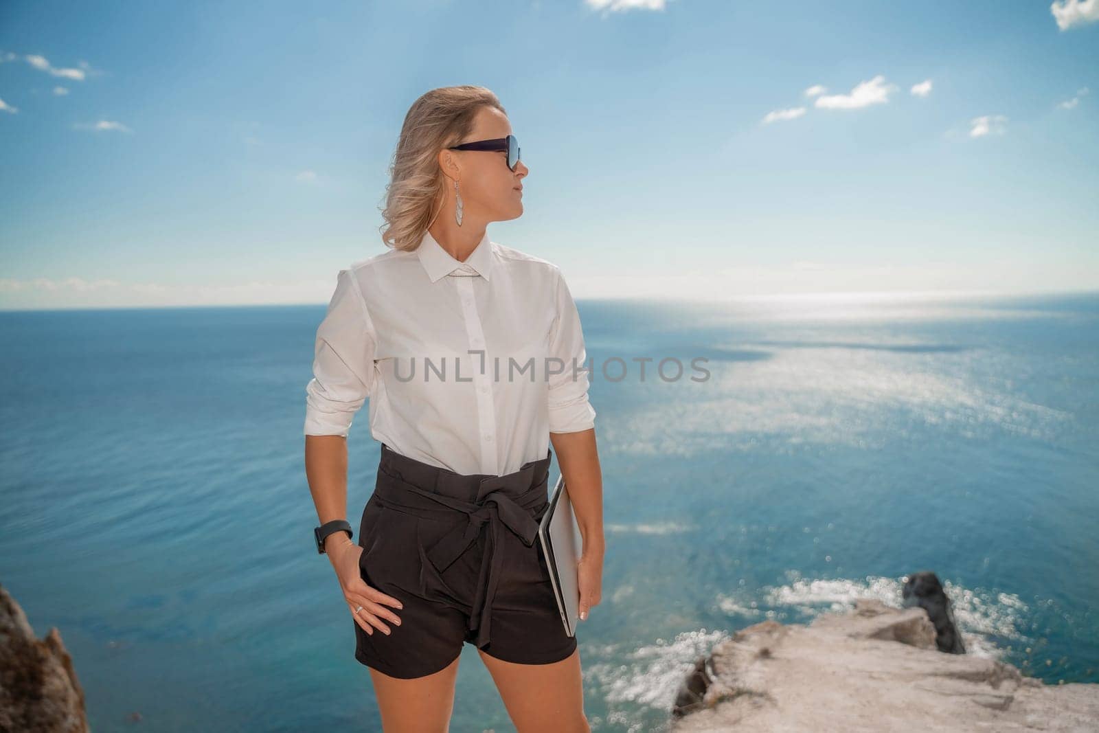 Freelance women sea working on a computer. Pretty middle aged woman with computer and phone outdoors with beautiful sea view. The concept of remote work. by Matiunina