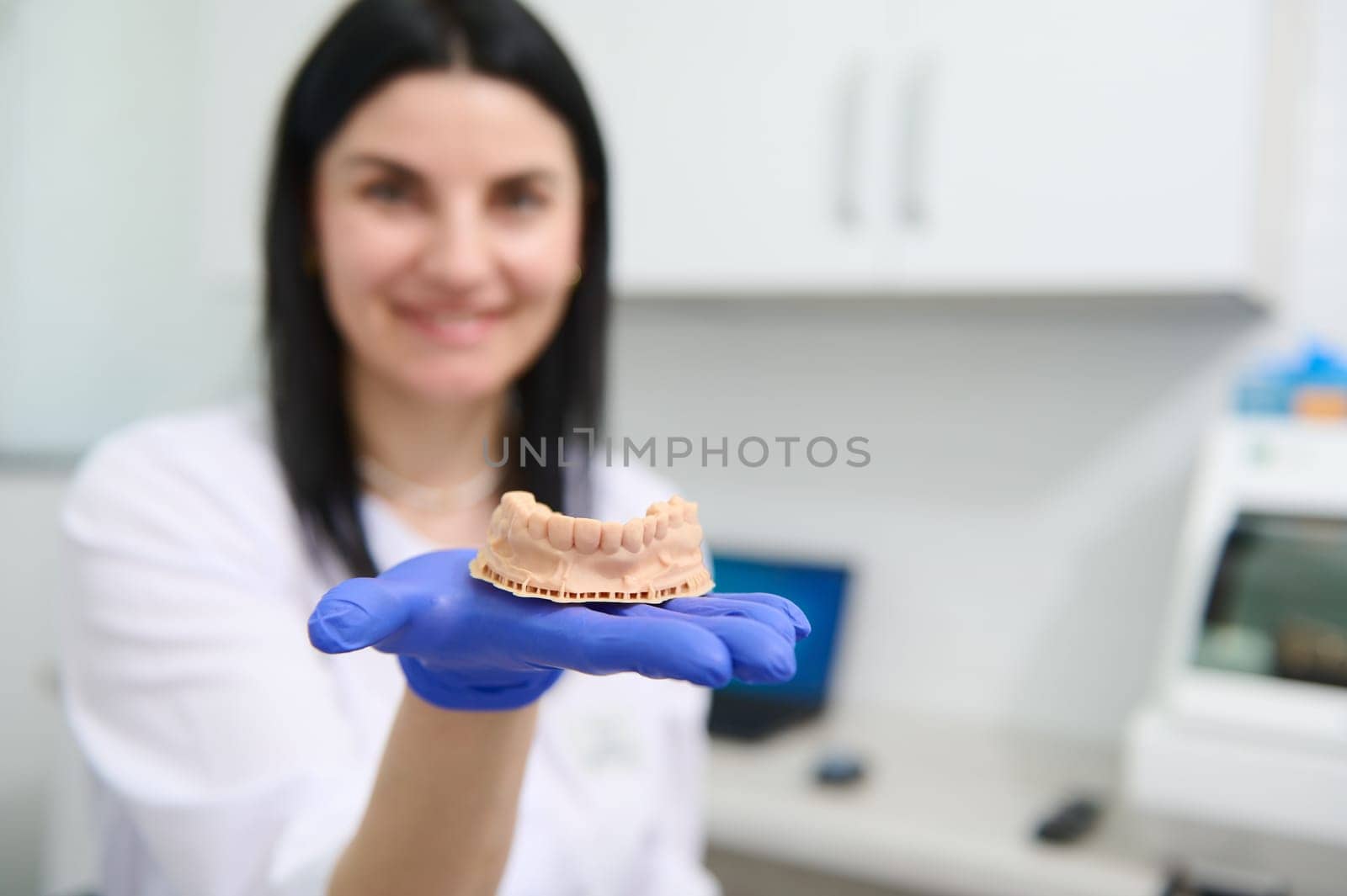Details: gypsum mold of the human lower jaw in the hand of a blurred smiling female dentist, dental technician. by artgf