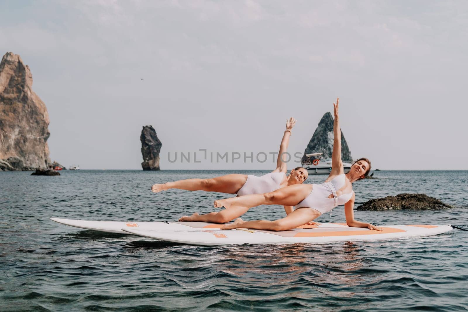 Woman sup yoga. Middle age sporty woman practising yoga pilates on paddle sup surfboard. Female stretching doing workout on sea water. Modern individual hipster outdoor summer sport activity