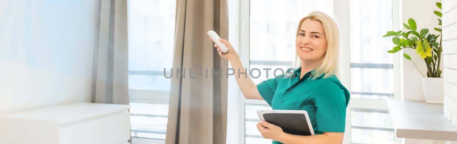 Portrait Of A Happy Woman Holding Remote Control In Front Of Air Conditioner At Home.
