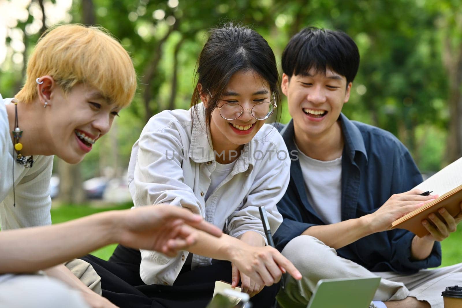 Group of happy students reading book, working on group project while sitting in university yard. Education and youth lifestyle concept.