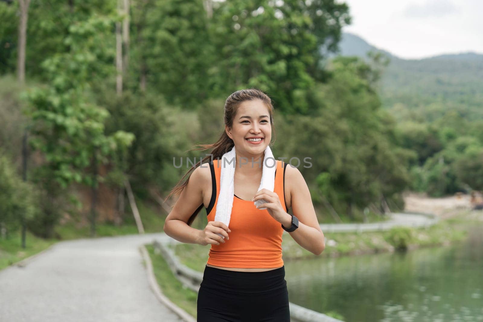 Happy woman wearing sportswear jogging in the park. Young beautiful asian female in sports bra running outdoor. Workout exercise in the morning. Healthy and active lifestyle concept.