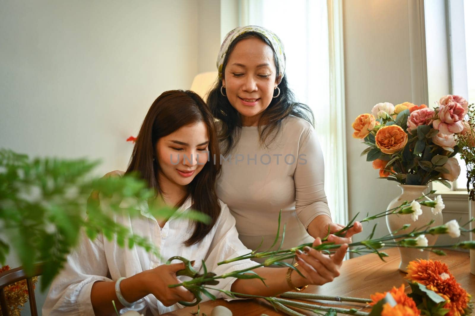 Family and leisure activity concept. Shot of senior woman and adult daughter creating beautiful bouquet in living room by prathanchorruangsak