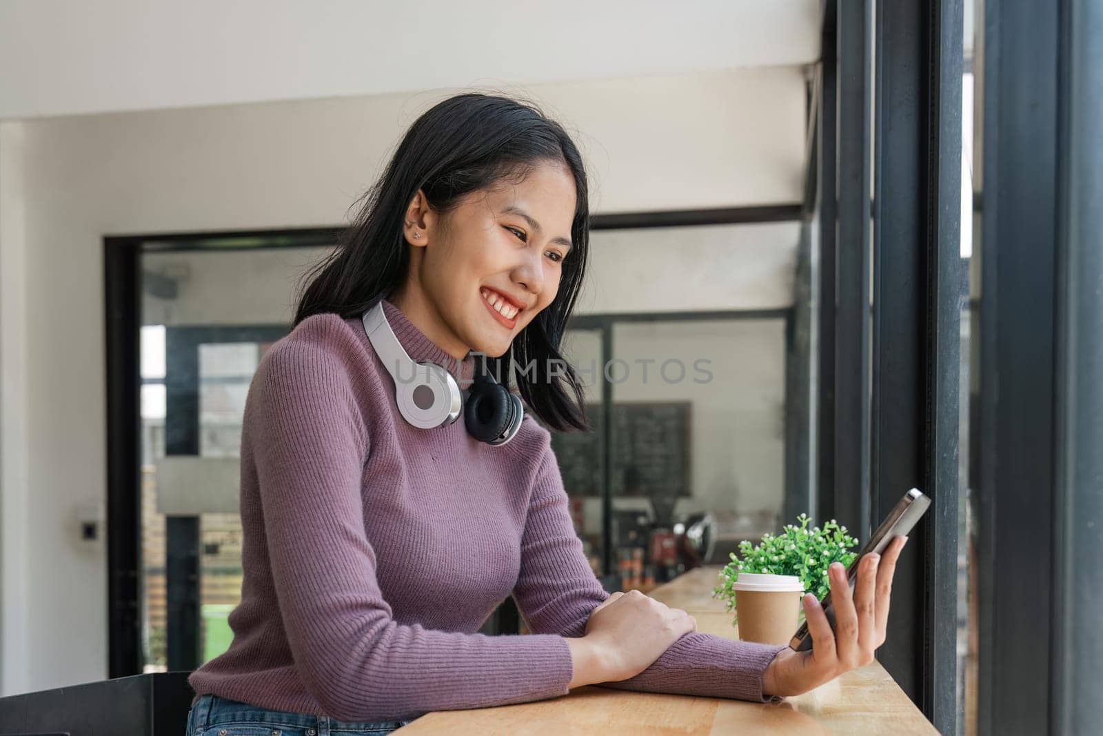 Beautiful young woman holding smart phone and looking at smart phone with smile while sitting in comfortable chair.