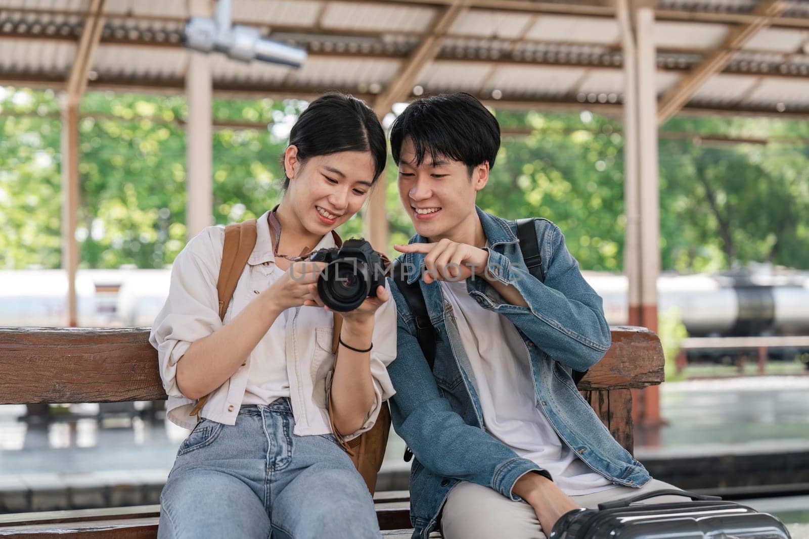 Beautiful couple at railway station waiting for the train. A young woman and a man are sitting and looking at pictures taken by cameras at a train station by nateemee