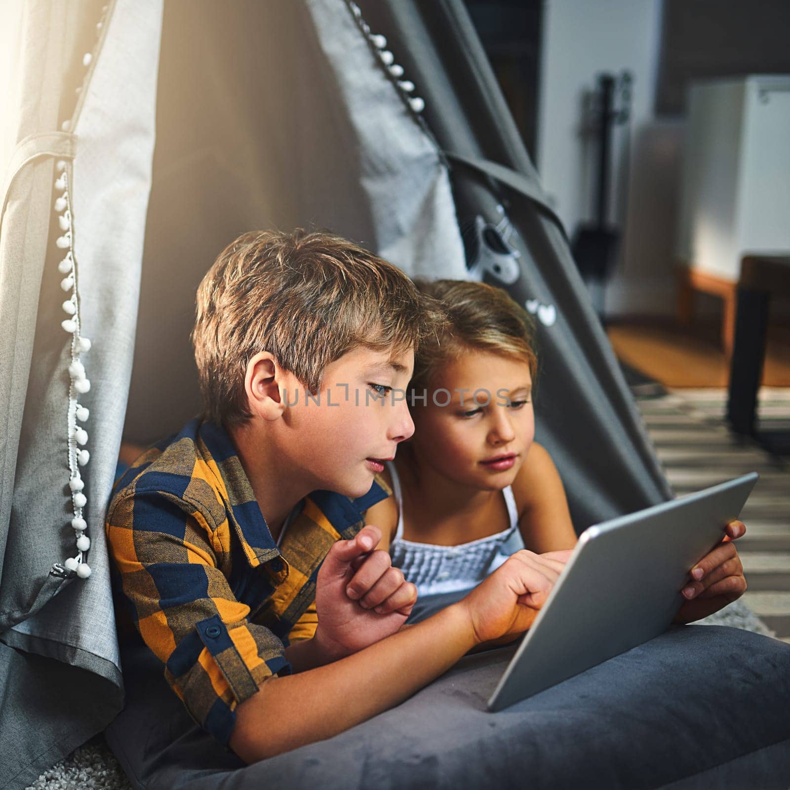 Siblings having fun on the wifi. an adorable little boy and girl using a tablet together while chilling in a homemade tent in the living room at home