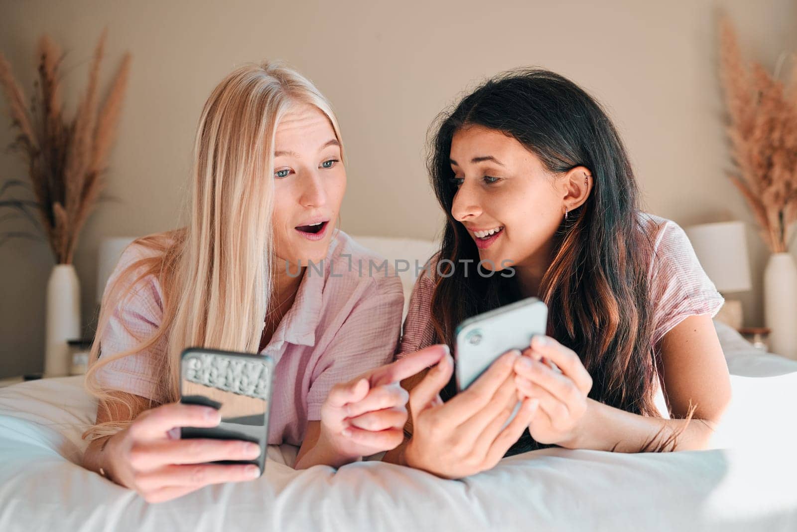 Wow, happy and women with a phone on a bed for social media, communication and notification. Shock, smile and friends reading news, message or online chat on a mobile during a sleepover together.
