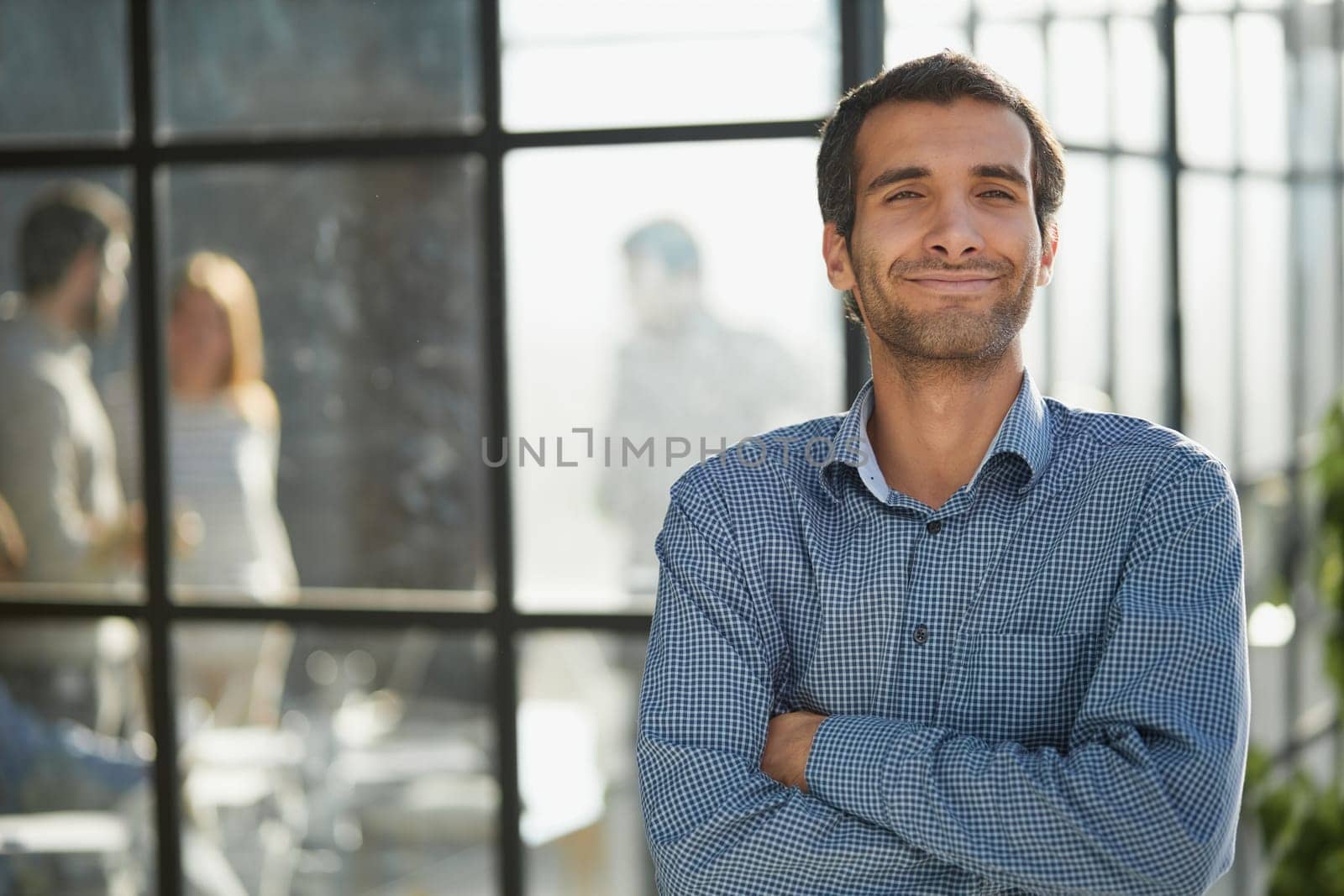 Middle aged white male creative in casual office lounge area looking to camera, arms crossed, waist up
