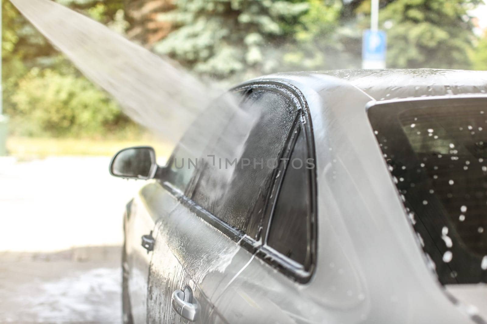 Side window of car washed in self serve carwash, high pressure jet water spraying on glass.