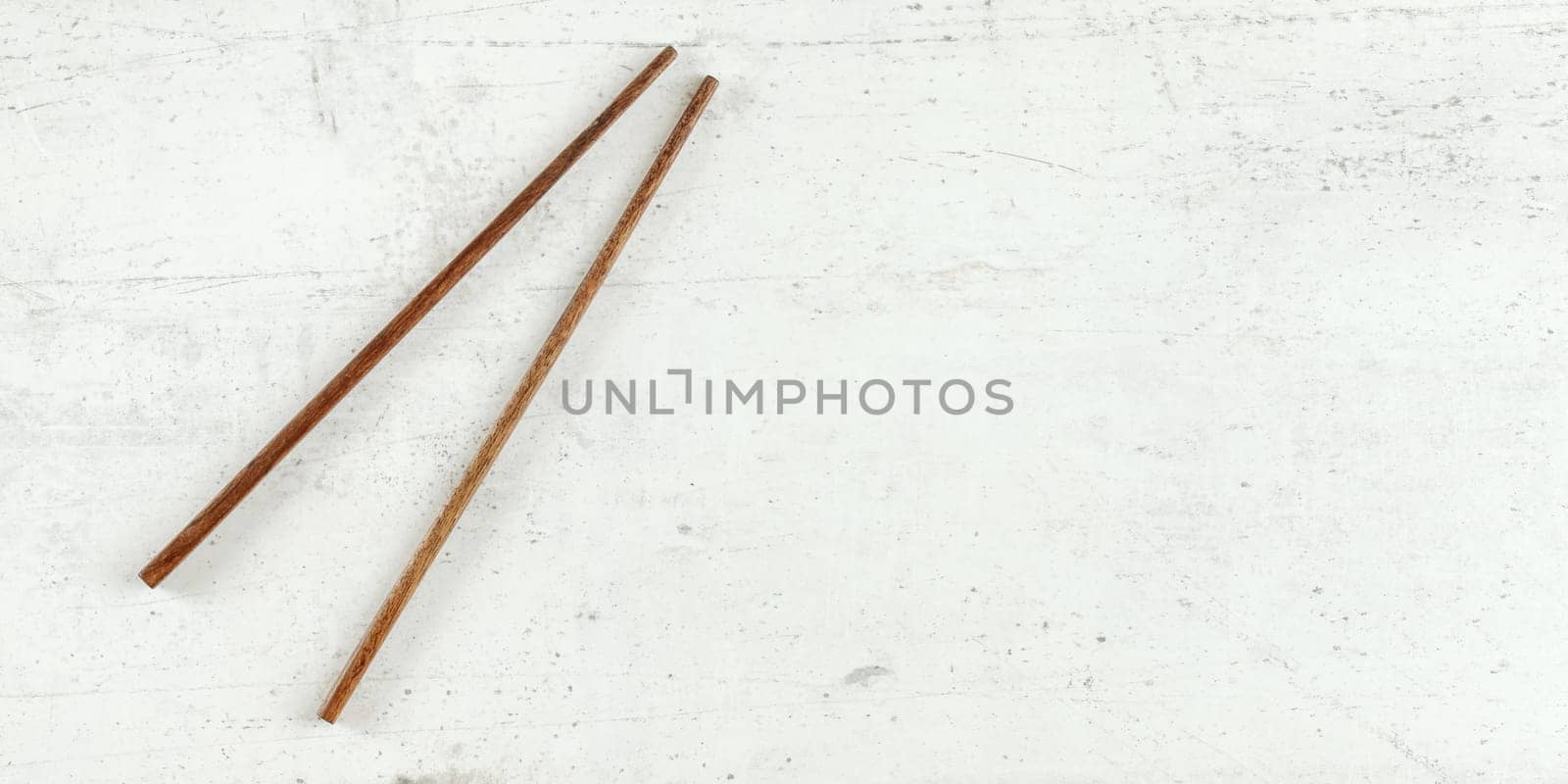 Top down view - pair of dark wood chopsticks on white board. Can be used as banner for asian / chinese food, space for text on right.