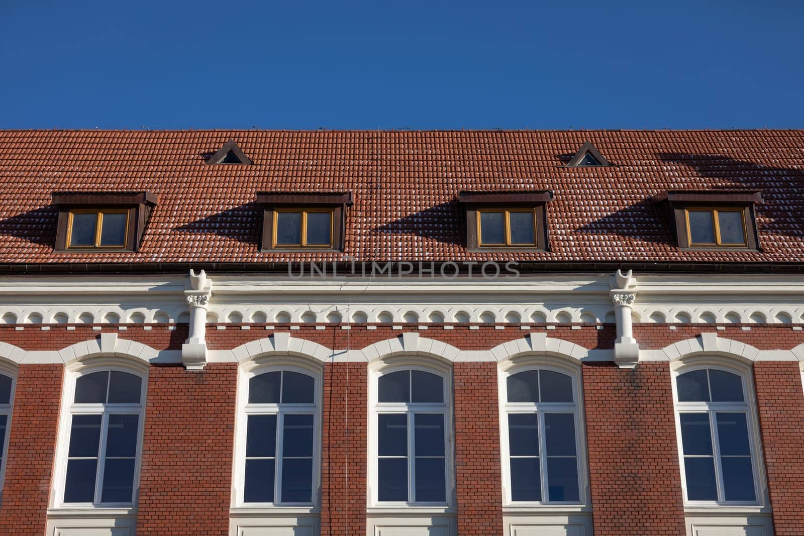 Front view of the curtain wall and roof. Entire building made of red brick and red tile. Clear blue sky.