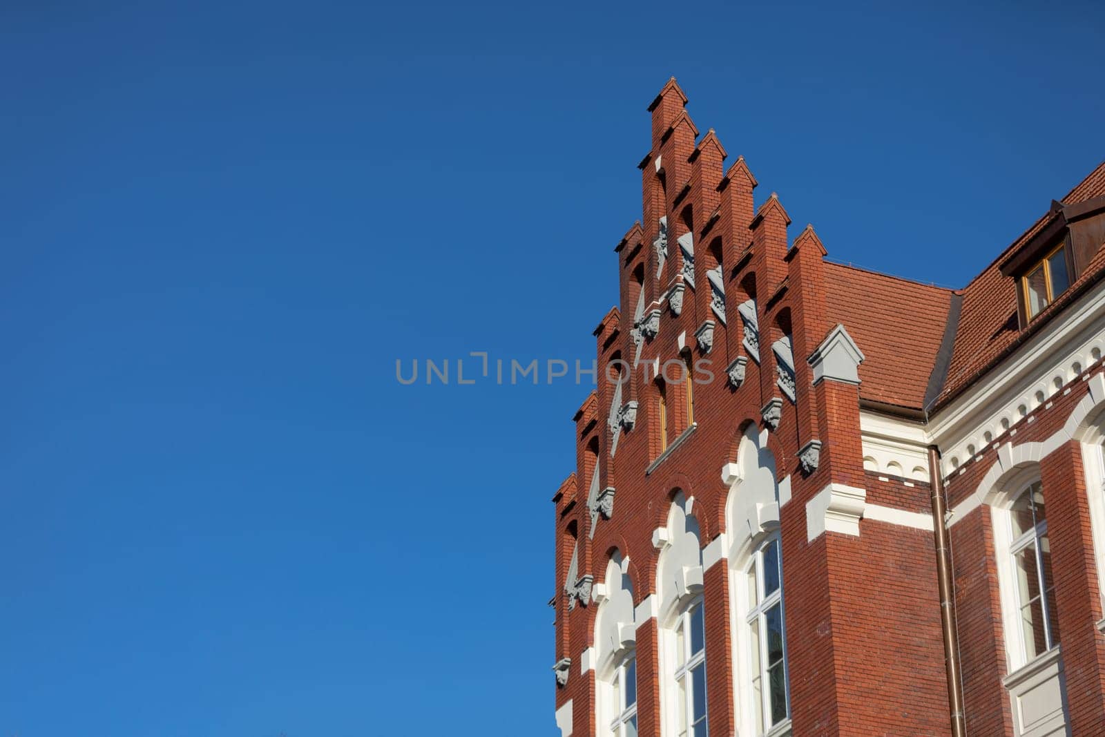 View from the bottom of the red brick building, richly decorated and maintained in neo-Gothic style. Clear blue sky.