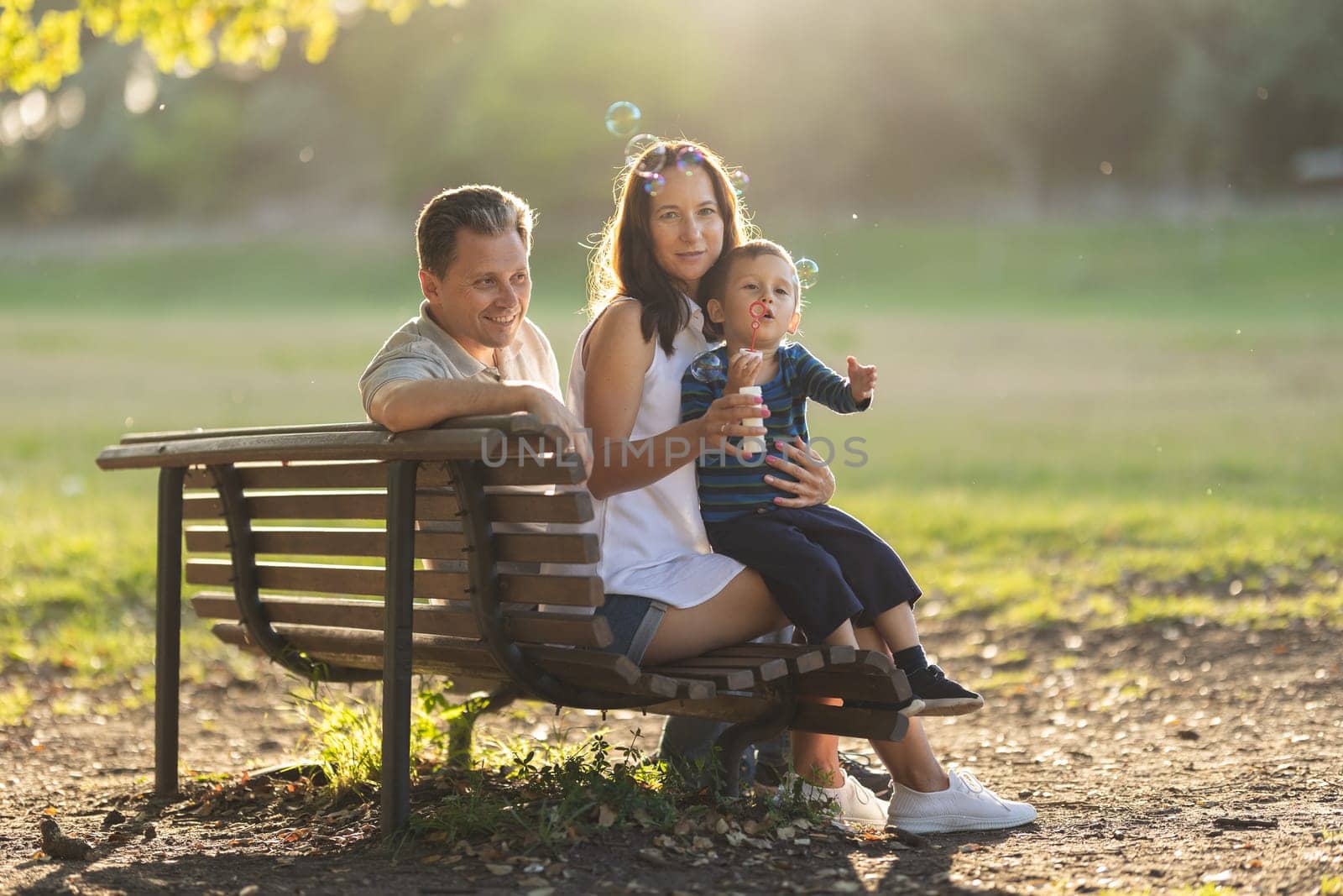 Cute white family sitting on a bench in the park. Mid shot