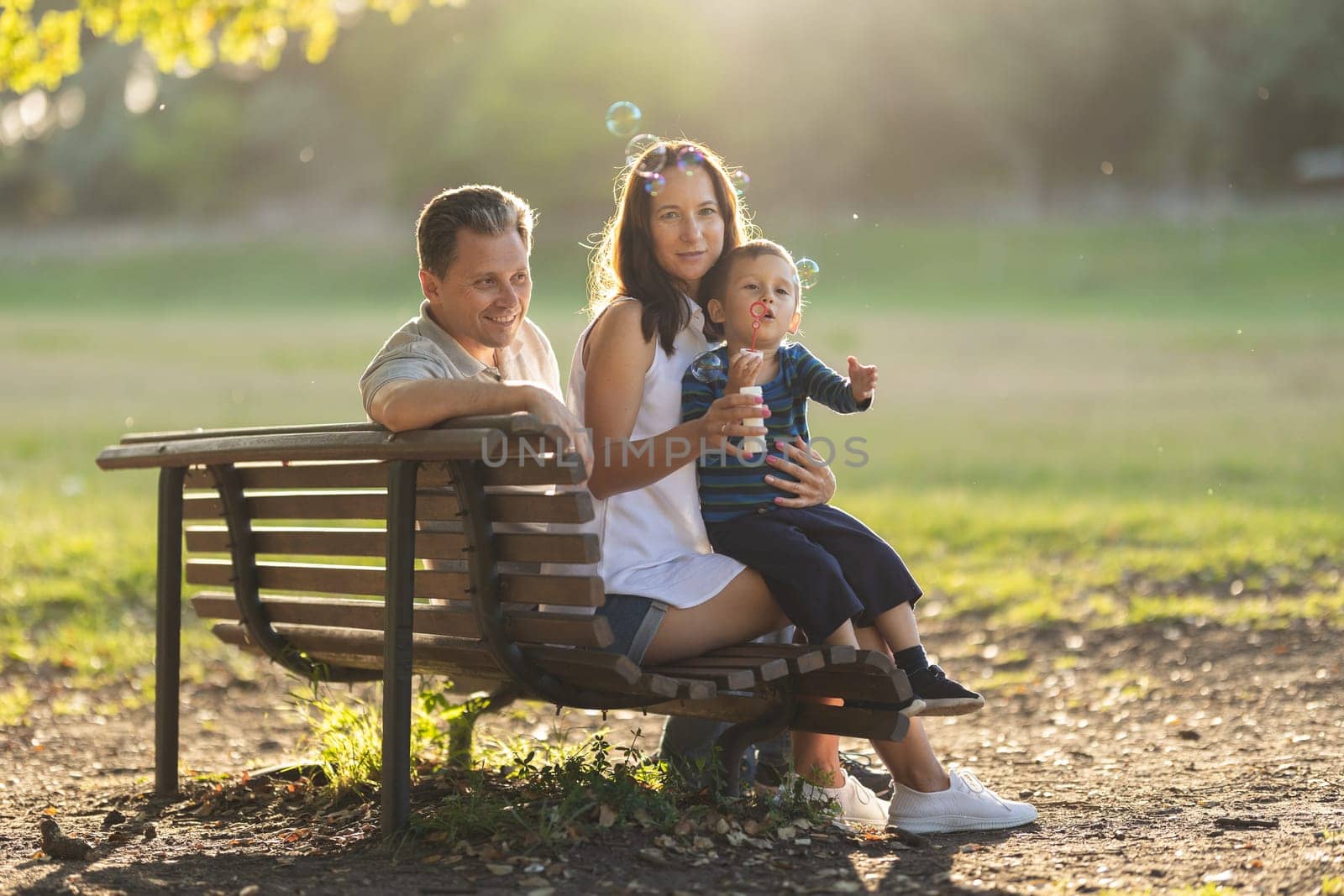 Cute white family sitting on a bench in the park. Mid shot
