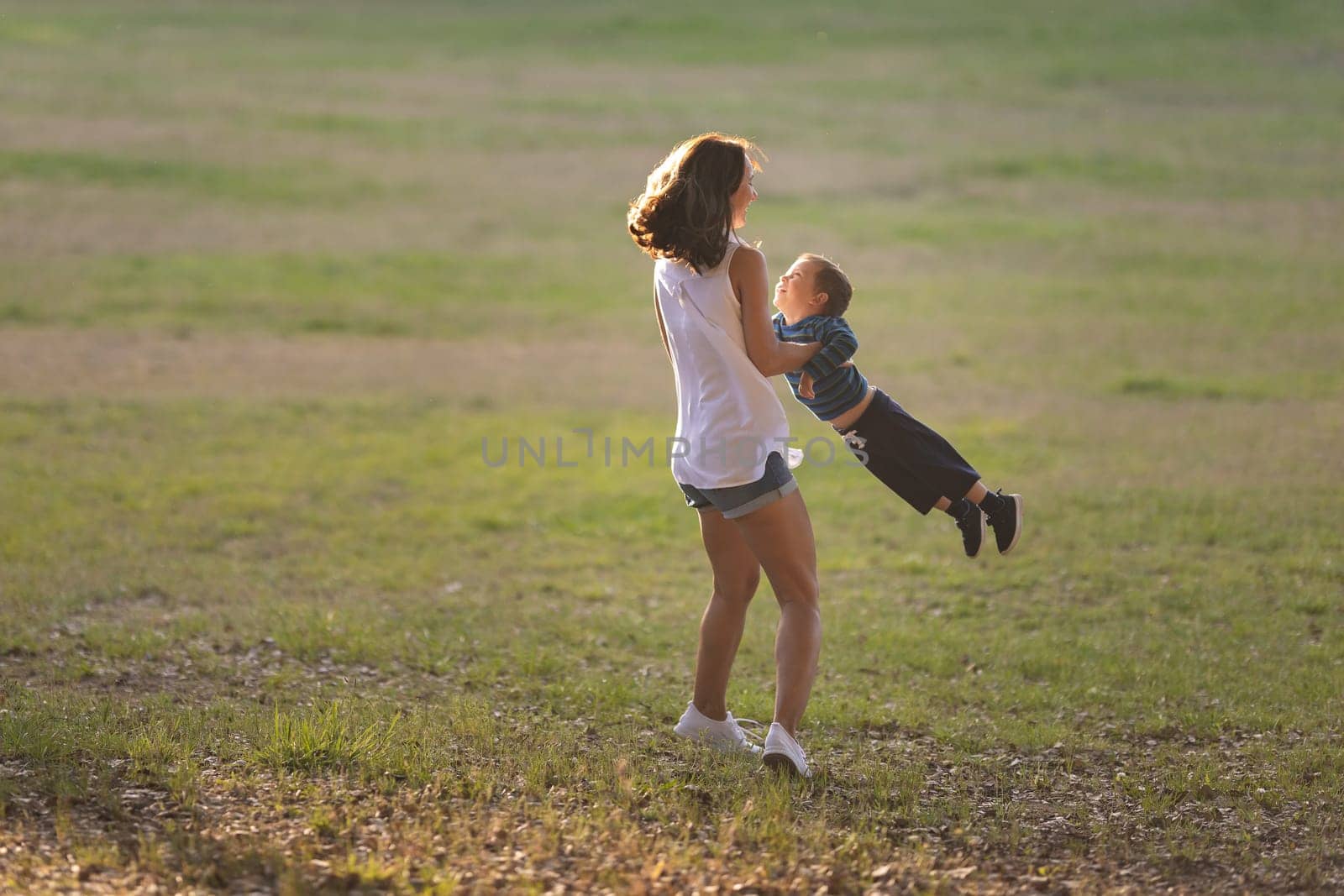 Happy motherhood - Mom spins her little son in the field. Mid shot