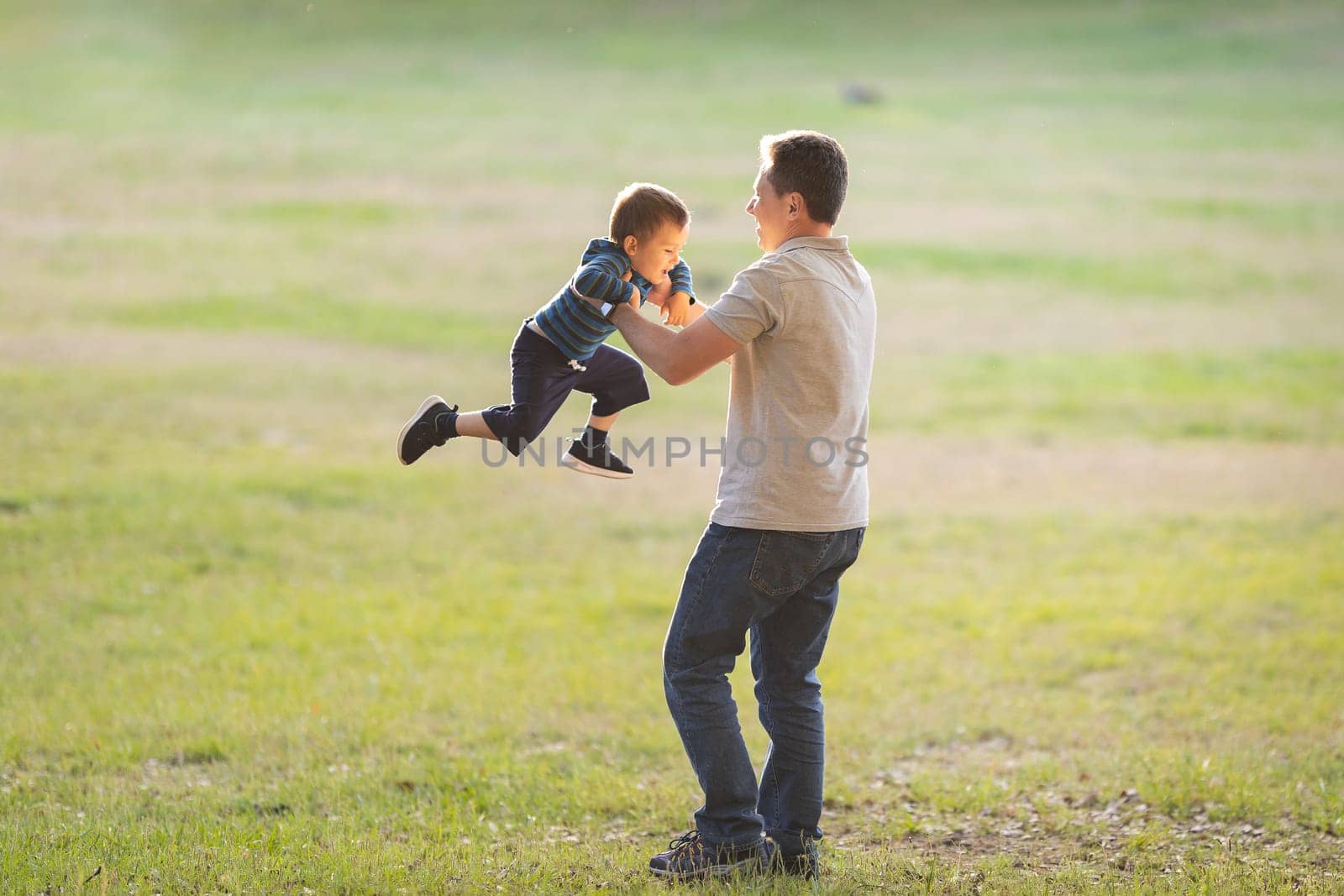 Happy fatherhood - dad spins his little son in the field. Mid shot