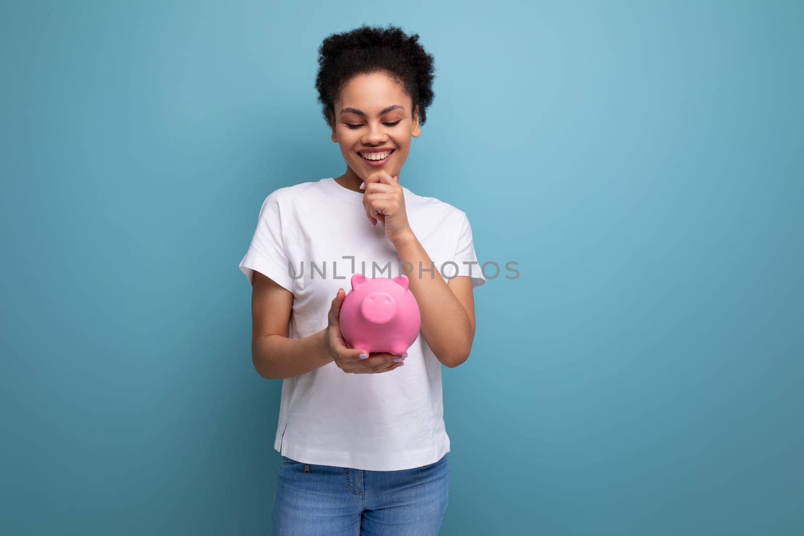 young latin brunette student woman in a white t-shirt keeps savings in a piggy bank by TRMK