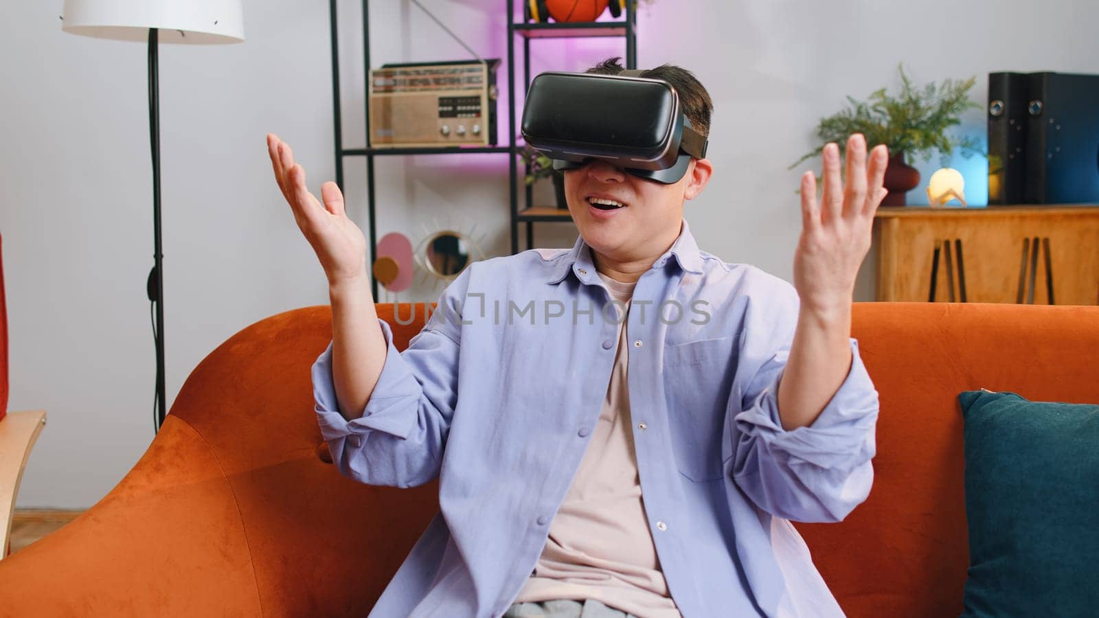Asian man using virtual reality futuristic technology VR app headset helmet play simulation 3D 360 video game watching film movie at home apartment. Guy in goggles sits on sofa. Transition zoom effect