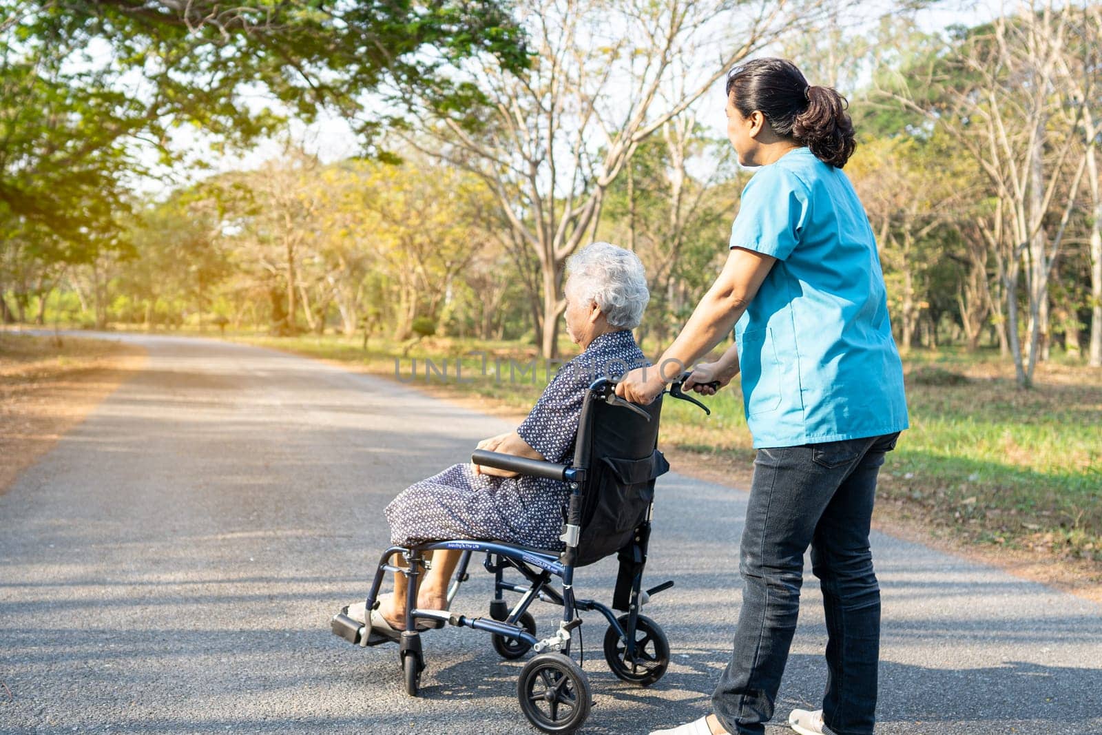 Caregiver help and care Asian elderly woman on wheelchair at park with happy in holiday. by pamai