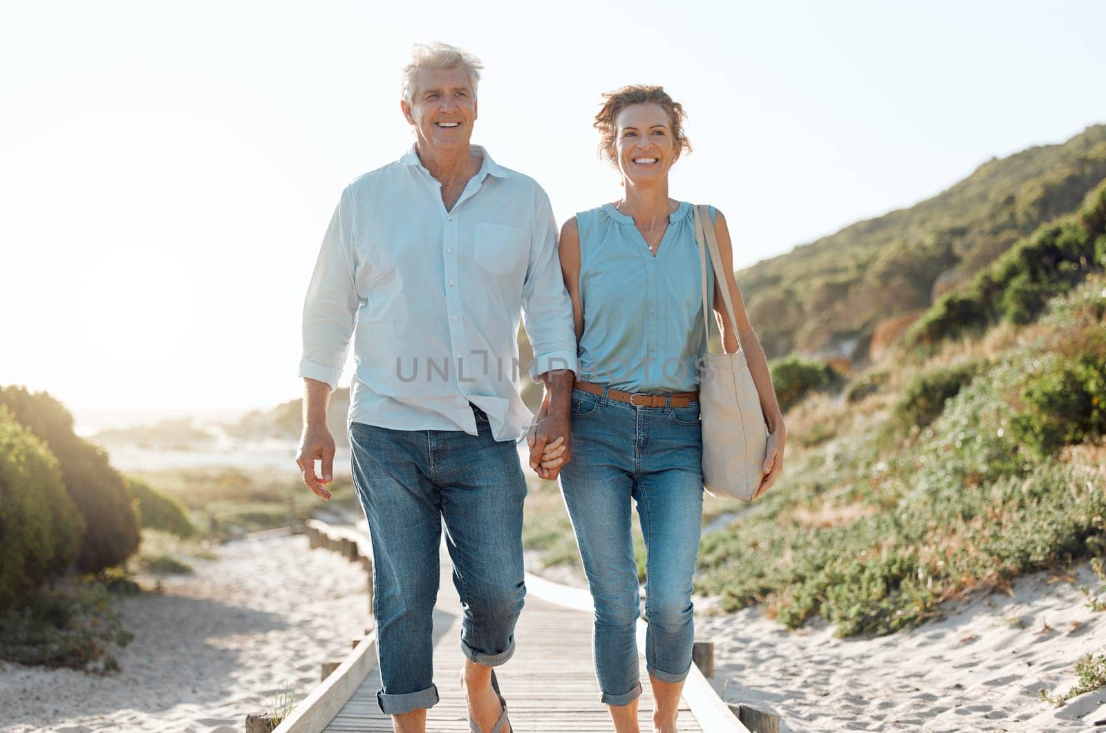 Senior, couple and walking at the beach with hands in portrait for happiness on a vacation in the outdoor. Mature, woman and man holding by ocean for travel on holiday with sunshine for the weekend. by YuriArcurs