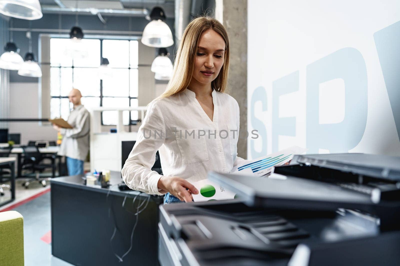 Young employee using modern printer in office by Fabrikasimf