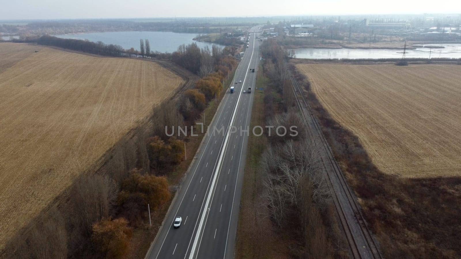 Large plowed field with plowed land and yellow dry straw after harvesting wheat, a lake, a highway with driving cars on an autumn day. Agro industrial agricultural farm landscape. Aerial drone view.