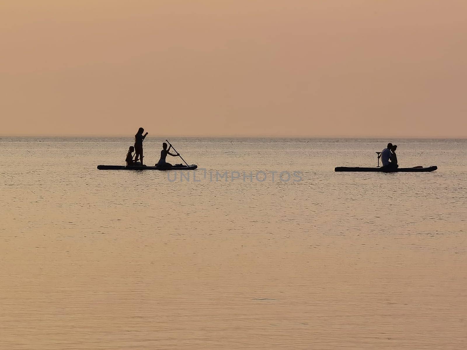 Group of people on stand up paddle board at quiet sea on sunset or sunrise. People on sup board and bright sunset by sarymsakov